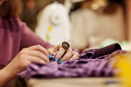 Female hands sewing cloth with needle at seamstress workplace. Side viewの写真素材