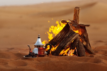 Dates, teapot, cup with tea near the fire in the desert with a beautiful backgroundの写真素材
