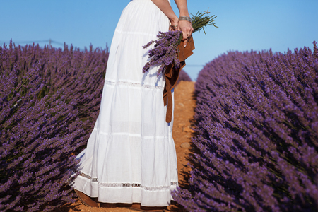 Beautiful girl in a white dress and hat in the style of boho in a lavender field with a bouquet of lavenderの写真素材