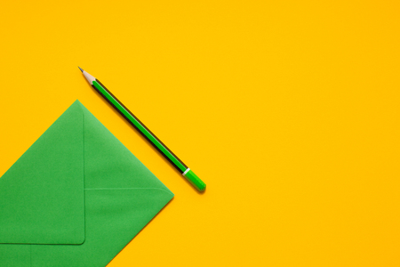 Green envelope and simple green pencil on a yellow background, top view, with space for text.