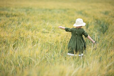 Happy girl walking in golden wheat, enjoying the life in the field. Nature beauty and field of wheat. Family outdoor lifestyle. Freedom concept. Cute little girl in summer fieldの写真素材