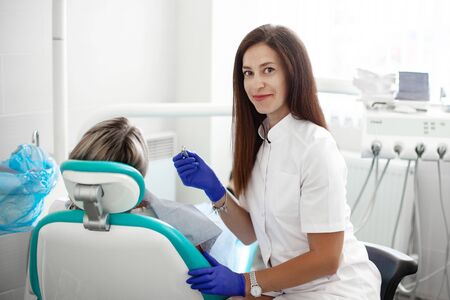 A young girl dentist treats a patient. A woman is sitting in a dental chair in the clinic. Medicine, health, dentistry concept.の写真素材