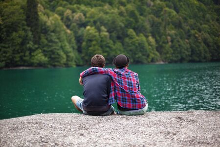 Young stylish couple of travelers looks at a mountain lake. Travel and active life concept.の写真素材