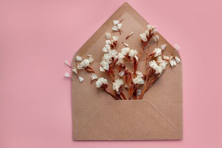 Flowers in an open envelope from kraft paper on a pale pink background. The message of Valentine's Day, Women's Day, wedding. Flat lay, top viewの写真素材