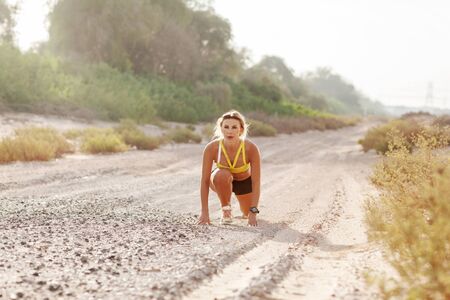 A young slender woman in sportswear is preparing to run from a low start. Fitness, healthy lifestyle