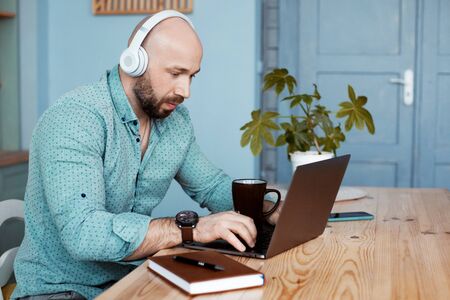 An adult man is drinking coffee and typing on a laptop. The businessman works at home during...