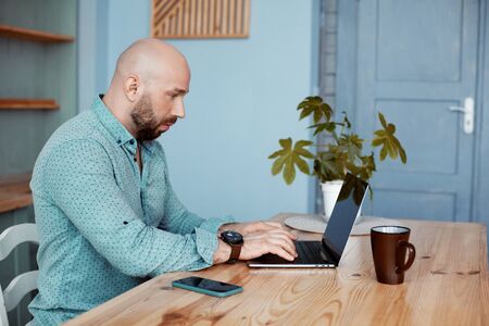 An adult attractive man works at the computer during morning coffee. Businessman typing on a laptop...