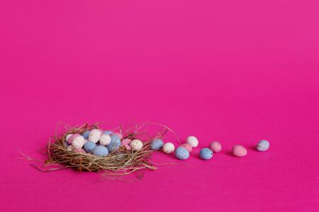 Bright colorful Easter eggs in a bird's nest on a pink background with space for text. The concept...