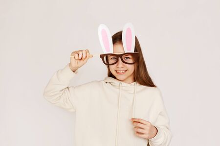 A young girl in a mask-glasses with rabbit ears on a light background with space for text. Preparing...