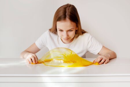 The charming girl smiles and makes a bubble of yellow slime. A child plays with slime. Toys from the slimeの写真素材