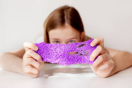 A beautiful girl stretches the purple slime to the sides and hides behind it. Children's hands play with a slimy toy. Selective focus. Anti-stress toyの写真素材