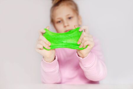 Cute girl playing with green slime. The girl holds in her hands and stretches the mucus . Slime toy, anti-stress toyの写真素材