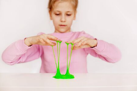 A charming girl holds a hand-made toy called slime. A child plays with green sticky slimeの写真素材