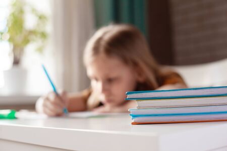 A beautiful girl writes with a pen in a notebook. The child performs homework. Home training, online trainingの写真素材