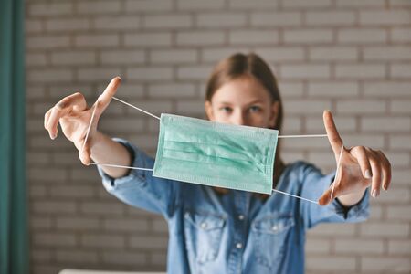 A beautiful teenage girl holds a protective medical mask in her hands. Protection, prevention