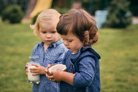 Two little girls holding a glass of coconut milk and coconut in their hands. Healthy and wholesome food.の写真素材