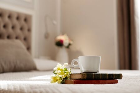 Books, flowers, and a coffee Cup lie on the bed. Romantic gift, romantic message, coffee in bedの写真素材