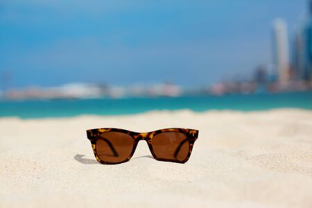 Sunglasses lie on a white sandy beach against a blue sea and sky. Side view, space for text