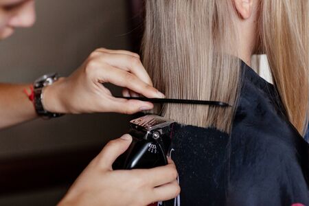A hairdresser makes a fashionable haircut for a girl with a comb and a clipper
