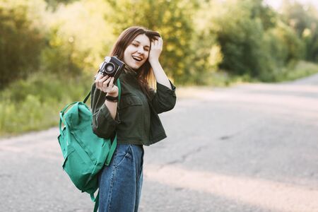 A smiling girl holds a camera in her hands. The girl travels and takes photos of landscapes on a...