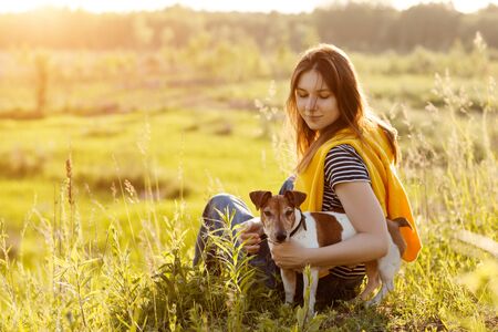 A beautiful young girl is sitting on the grass and hugging her dog. A girl and her pet are resting after a walk in nature. Friend, Friendship, Care. Space for textの写真素材