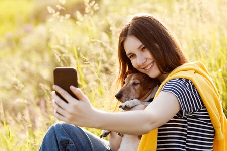 An attractive teen girl takes photos of herself and her dog using a mobile phone camera. A girl...