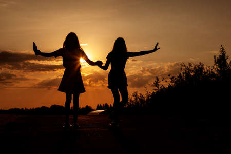 Two blond teenage girls ride skateboards at beautiful sunset.の写真素材