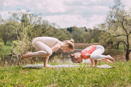 A beautiful young woman with her charming teenage daughter practices yoga outdoors in a Park. Side view, space for textの写真素材