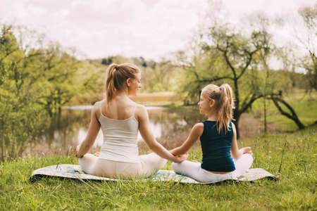 A beautiful young woman and a fair-haired girl are meditating in the Lotus position. Family vacation, meditation. Side view, space for textの写真素材