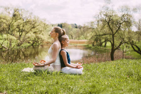 A beautiful young woman and a fair-haired girl are meditating in the Lotus position. Family vacation, meditation. Side view, space for textの写真素材