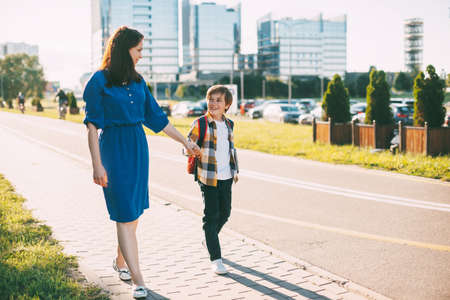 A mother walks her son to school. A cheerful smiling boy walks with his mother by the hand from...