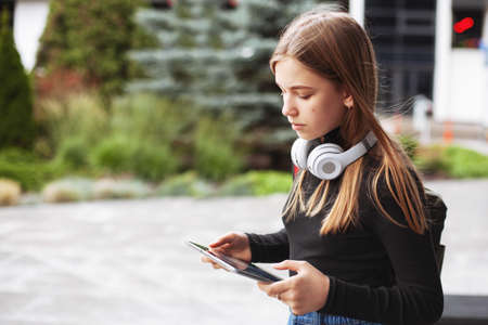 Beautiful fashionable schoolgirl studying online with tablet and headphones sitting on the steps...