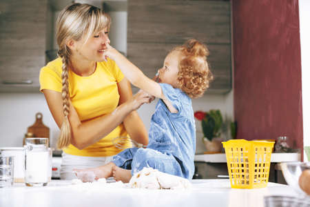 Mom and daughter are cooking in the kitchen, smiling and playing. On the table is the dough, there is kitchen equipment and milk.の写真素材