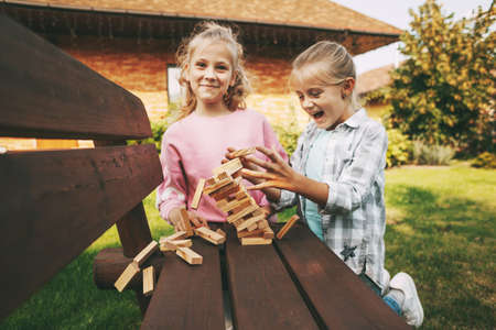Two girls are having fun and playing a wooden board game outdoors near their home.の写真素材