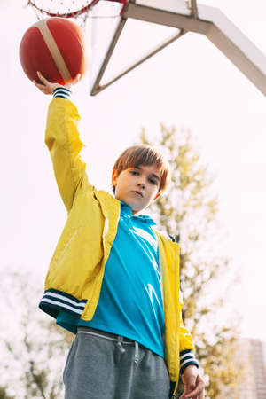 Portrait of a cute boy basketball player standing with a ball in his hands next to the basketball...