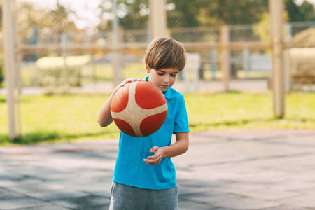 Focused cute boy athlete leads the ball in a game of basketball. A boy plays basketball after school. Sports, healthy lifestyle, leisureの写真素材