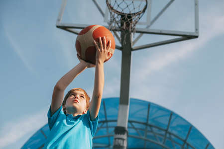 A boy in a sports uniform throws a ball into a basketball basket. A child plays basketball. Sports,...