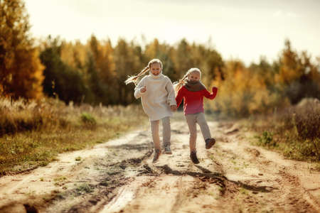 Two sisters in warm sweaters hug and run along the trail in the autumn forest.の写真素材