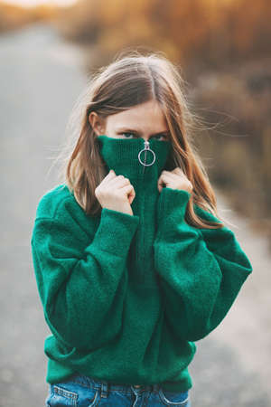 Beautiful teenage girl with blonde hair and blue eyes in a warm green sweater in an autumn park.の写真素材