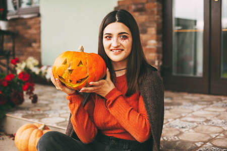 A beautiful girl with dark hair with makeup for the celebration of Halloween holds a pumpkin in her hands and smiles.の写真素材