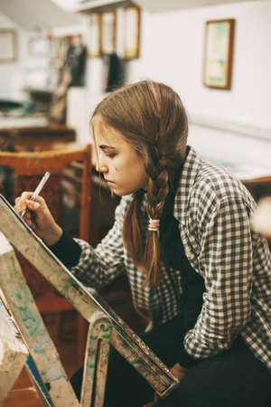 Beautiful teenage girl at art school painting on easel, creativity concept,の写真素材
