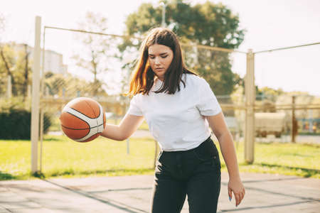 Young cute teen girl leads the ball in a basketball game. A girl plays basketball after school....