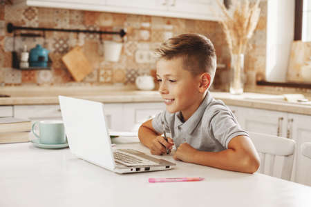 Boy does homework in the kitchen with a laptop online, talking to the teacher. Distance learning, online education,の写真素材