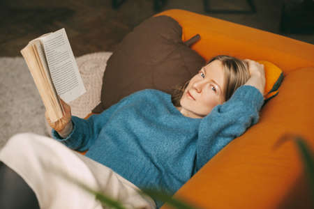 A beautiful girl is relaxing on the sofa in the living room, reading her favorite novel. Cute,...