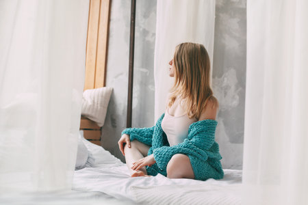 Cute girl sitting cross-legged on the bed in the morning. Young woman in pajamas sitting on the bed after waking up.の写真素材