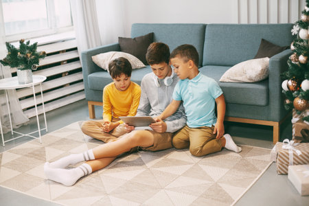 Smiling teenage boys communicate with friends online using a tablet. Young people congratulate friends and relatives on Christmas and New year.の写真素材