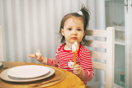 Charming little girl sitting at the table with a spoon in her hand waiting for Christmas DINNER.の写真素材