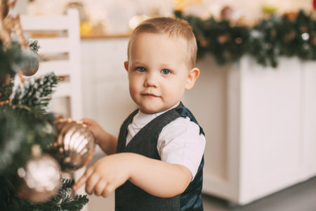 A funny little boy in a suit is decorating the Christmas tree. Holiday, event, Christmas and New yearの写真素材