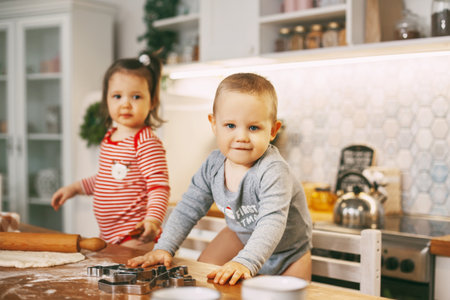 The kid and his little sister are preparing Christmas cookies in the kitchen, there is dough and a rolling pin on the table. Preparing for Christmas and New yearの写真素材