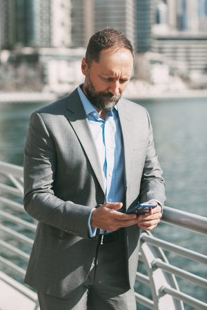 Young businessman with a phone in his hands, standing in a big city among high-rise buildingsの写真素材